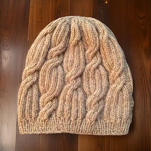 May include: A beige knitted hat with a cable knit pattern.