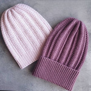 Könnte beinhalten: Zwei Strickmützen, eine rosa und eine lila, mit gerippter Struktur.