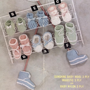 May include: A set of 10 knitted baby booties in various colours, including pink, blue, and green. The booties are displayed on a white wire rack. The text "SUNSHINE BABY WOOL 3 PLY, MAJESTIC 3 PLY OR BABY NYLON 3 PLY" is printed below the rack.