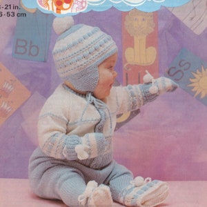 Può includere: Un bambino che indossa un completo di maglia blu e bianco con un cappello e guanti abbinati. Il completo ha un motivo a righe e pompon sul cappello e sui guanti. Il bambino è seduto su una superficie rosa. 18-21 pollici. 46-53 cm