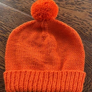 Peut inclure: Un bonnet en tricot orange vif avec un pompon moelleux sur le dessus.