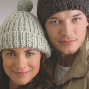 May include: A close-up of two people wearing knitted hats. The woman is wearing a light green hat with a pom-pom on top. The man is wearing a dark grey hat. Both hats have a ribbed texture.