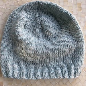 May include: A light blue knitted beanie hat. The hat is made of a soft, textured yarn and has a simple, classic design.