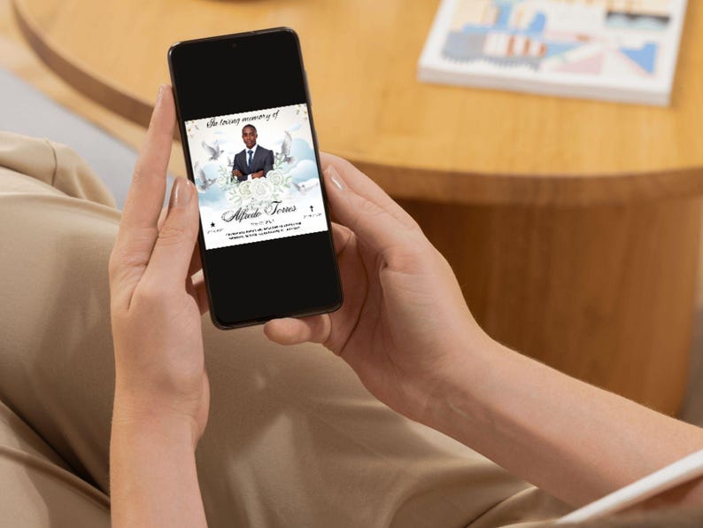 Pu&ograve; includere: Uno smartphone che mostra un biglietto di memoria digitale con una foto di un uomo in abito e cravatta. Il biglietto ha uno sfondo bianco con colombe e nuvole. Il testo sul biglietto recita "In memoria affettuosa di" e "Alphonso Jones".