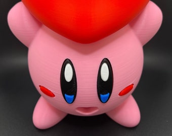 May include: A pink and red 3D printed figurine of a cartoon character with large eyes and a heart-shaped head.