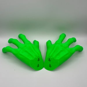 May include: A pair of bright green, three-fingered hand sculptures. Each hand features a textured, claw-like appearance with prominent knuckles and veins. The base of each hand is flat and includes two integrated keyhole slots for wall mounting.