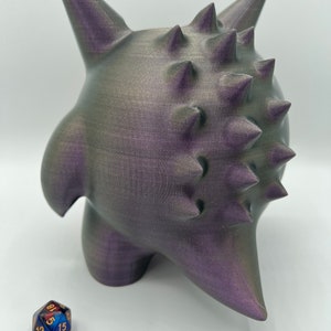 K&ouml;nnte beinhalten: Eine 3D-gedruckte, violette und graue, stachelige Kreatur mit einer strukturierten Oberfl&auml;che. Die Kreatur steht auf einer wei&szlig;en Oberfl&auml;che.