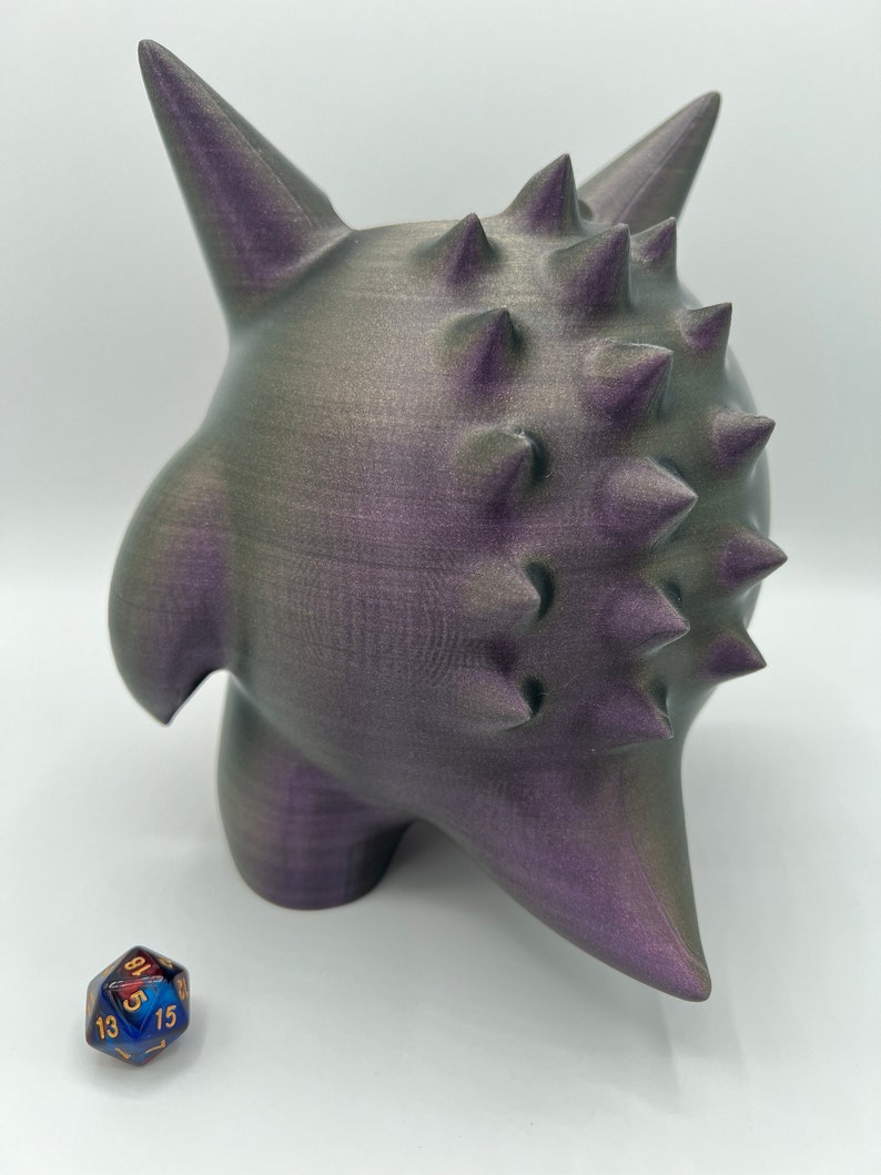 K&ouml;nnte beinhalten: Eine 3D-gedruckte, violette und graue, stachelige Kreatur mit einer strukturierten Oberfl&auml;che. Die Kreatur steht auf einer wei&szlig;en Oberfl&auml;che.
