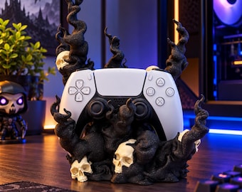 May include: A white video game controller resting in a black stand featuring sculpted skulls and swirling smoke-like tendrils. The base is dark and textured, with multiple off-white skulls integrated into the rising, organic black forms.