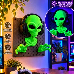 May include: A bright green alien head and hand wall mount attached to a black pegboard. The alien figure features large black oval eyes and is wearing black over-ear headphones. The text UV REACTIVE GLOWS UNDER BLACKLIGHT is visible.