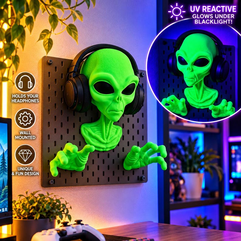 May include: A bright green alien head and hand wall mount attached to a black pegboard. The alien figure features large black oval eyes and is wearing black over-ear headphones. The text UV REACTIVE GLOWS UNDER BLACKLIGHT is visible.