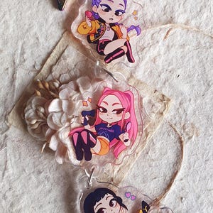 Op de afbeelding: Duidelijke acryl sleutelhangers met illustraties van anime-personages. De bovenste sleutelhanger heeft een personage met paars haar en een gele jas. De middelste sleutelhanger heeft een personage met roze haar. De onderste sleutelhanger heeft een personage met zwart haar.