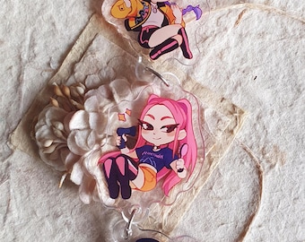 Pode incluir: Chaveiros de acrílico transparente com ilustrações de personagens em estilo anime. O chaveiro superior apresenta um personagem com cabelo roxo e uma jaqueta amarela. O chaveiro do meio tem um personagem com cabelo rosa. O chaveiro inferior tem um personagem com cabelo preto.