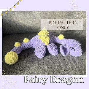 May include: A purple and yellow crocheted fairy dragon plush toy. The toy is lying on a gray couch. The text "PDF PATTERN ONLY" is written in brown text on a white background. The text "Fairy Dragon" is written in black text on a white background.