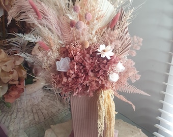 Arreglo floral de flores secas, tonos neutros tierra rosados, jarrón grande arqueado.