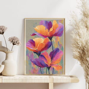 Könnte beinhalten: Ein gerahmter Kunstdruck mit drei großen, stilisierten Blumen. Die Blütenblätter sind eine lebendige Mischung aus Orange- und Lilatönen, vor einem gedämpften Hintergrund mit bunten Pinselstrichen. Das Kunstwerk wird in einem hellen Holzrahmen präsentiert.