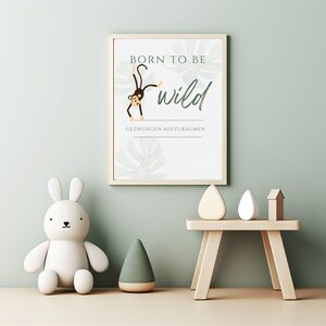 May include: A framed print with the words "Born to be wild" and a cartoon monkey illustration. A white bunny toy, a green cone, and a small wooden table with decorative objects are in the foreground. The background is a light green wall.