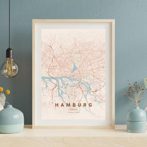 Könnte beinhalten: Gerahmter Karten-Druck von Hamburg, Deutschland. Die Karte zeigt ein Straßennetz und Wasserwege in Braun- und Blautönen auf cremefarbenem Hintergrund. Der Name der Stadt ist in einer fetten, braunen Schrift dargestellt.