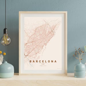 May include: Framed map print of Barcelona, Spain, in a minimalist style. The map features a network of roads and streets in a reddish-brown hue against a cream background. The word "BARCELONA" is printed in a serif font.
