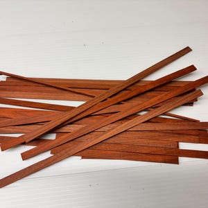 Könnte beinhalten: Ein Stapel dünner, rotbrauner Holzstreifen, wahrscheinlich zum Basteln oder Modellbau.