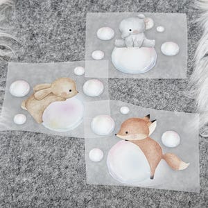 Könnte beinhalten: Aquarellillustrationen eines Kaninchens, eines Elefanten und eines Fuchses, jeweils auf einer großen, pastellfarbenen Blase sitzend. Die Tiere sind in sanften, natürlichen Farbtönen gehalten, umgeben von kleineren Blasen.