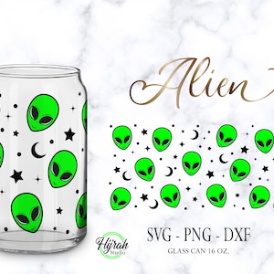 Może przedstawiać: Przezroczysty szklany kubek z wzorem zielonych twarzy kosmitów, czarnych gwiazd i księżyców. Słowo "Alien" jest napisane złotą czcionką. Szklanka ma pojemność 473 ml.