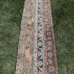 Pode incluir: Um tapete comprido e estreito com um design de patchwork. O tapete é composto por várias tiras de tecido diferentes, cada uma com um padrão único. O tapete é principalmente bege e marrom com detalhes em rosa, azul e verde.