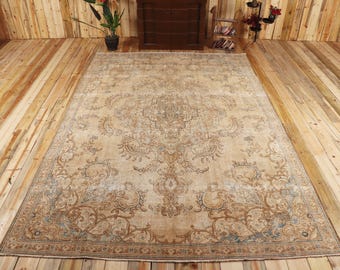 May include: A large rectangular area rug featuring a central medallion and intricate floral scrollwork patterns in shades of beige, tan, and muted blue. The rug has a detailed border with repeating motifs and a weathered, distressed appearance.