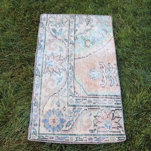 May include: A folded rectangular rug with a vintage design. The rug has a central peach-coloured field with floral patterns in blue, cream, and teal. The border is a darker blue with intricate designs. The rug is placed on green grass.