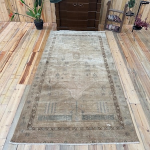 May include: A rectangular area rug featuring a faded beige and brown color palette with intricate geometric and floral patterns. The rug has a wide decorative border and a central medallion design, finished with short white fringe on both ends.