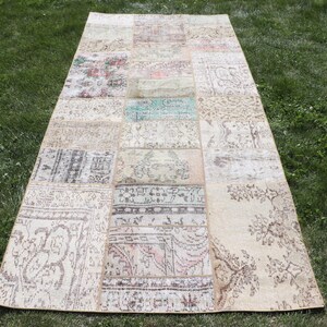 Puede incluir: Una alfombra vintage de patchwork con fondo crema y patrones marrones, azules y rosas. La alfombra está hecha de diferentes piezas de tela cosidas juntas.