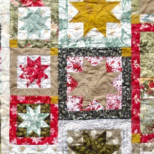 May include: A patchwork quilt with a variety of fabrics and colors, including red, green, brown, and white. The quilt is made up of squares and rectangles, and features a star pattern in the center.