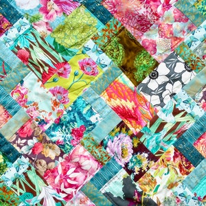 May include: A colourful quilt made of various floral patterned fabrics. The quilt is sewn in a diamond pattern with a light blue background. The quilt is made of a variety of fabrics, including floral prints, geometric patterns, and solid colours.