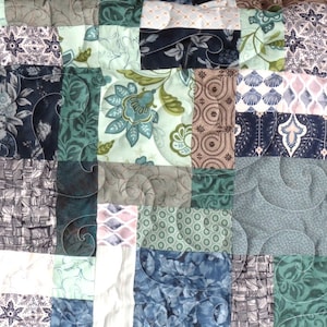 Könnte beinhalten: Eine Patchwork-Decke mit verschiedenen floralen und geometrischen Mustern in Blautönen, Grün- und Brauntönen. Die Decke besteht aus verschiedenen Stoffen und Texturen, was ein einzigartiges und interessantes Design ergibt.