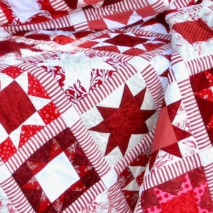 May include: A red and white patchwork quilt with a star design. The quilt is made of various fabrics, including stripes, polka dots, and floral patterns.