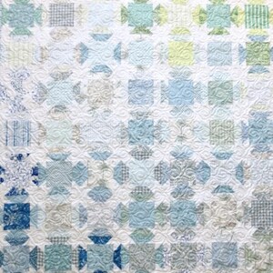 May include: A white quilt with a blue and green patchwork design. The quilt is made up of squares and rectangles of different sizes and colours. The quilt is quilted with a swirling pattern.