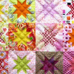 Könnte beinhalten: Eine Patchwork-Decke mit einer Vielzahl von bunten Stoffen und Sternmustern. Die Decke besteht aus Quadraten in verschiedenen Farben und Mustern, darunter Pink, Rot, Gelb, Grün und Orange. Die Sterne sind alle unterschiedlich groß und geformt, und einige sind weiß umrandet.