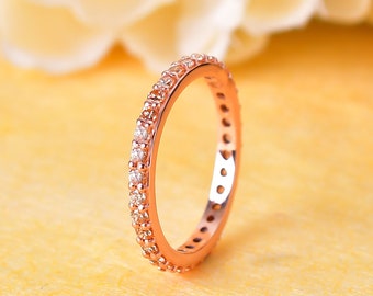 May include: A rose gold band ring with a row of small clear stones around the entire band.