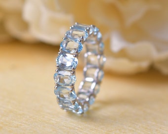 May include: A delicate eternity band ring with a row of oval-shaped light blue gemstones set in a silver band.