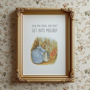 May include: A framed print with a gold ornate frame. The print features a watercolor illustration of rabbits in a forest scene, with the text "NOW RUN ALONG, AND DON'T GET INTO MISCHIEF" at the top. The background is a floral wallpaper.