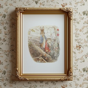 May include: A framed print featuring a classic illustration of a rabbit in a blue jacket and red bag, set in a garden scene. The print is in a gold ornate frame, adding a touch of vintage charm. The artwork is displayed against a floral wallpaper.