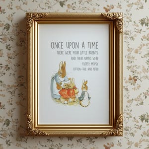 Puede incluir: Una impresión enmarcada con un marco dorado ornamentado, que presenta una ilustración infantil de conejos. La impresión incluye el texto "ONCE UPON A TIME" y los nombres de los conejos: Flopsy, Mopsy, Cotton-Tail y Peter.