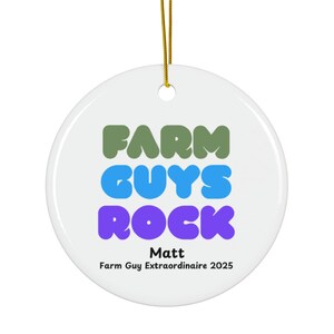 Könnte beinhalten: Runder, weißer Keramikschmuck mit dem Text "FARM GUYS ROCK" in Grün, Blau und Lila. Der Schmuck enthält auch den Namen "Matt" und den Satz "Farm Guy Extraordinaire 2025". Ein goldener Faden ist zum Aufhängen befestigt.