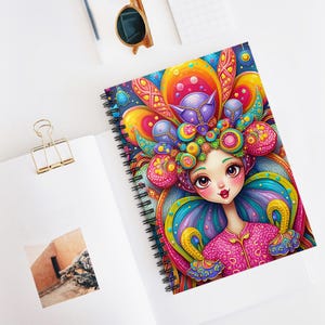 May include: A colorful spiral notebook featuring a whimsical illustration of a girl with large eyes and a vibrant, multi-colored headdress. The headdress is adorned with intricate patterns and swirls, creating a visually captivating design.