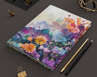 Könnte beinhalten: Ein Hardcover-Notizbuch mit einem lebendigen Blumendesign. Es zeigt orange, gelbe, blaue und lila Blumen in einem Aquarellstil auf weißem Hintergrund. Goldene und schwarze Bleistifte sowie goldene Büroklammern sind ebenfalls zu sehen.