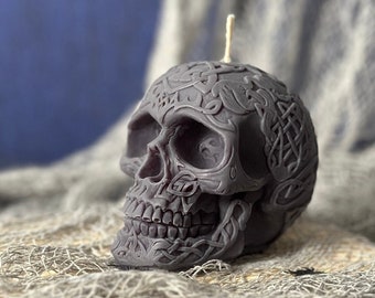 May include: A black skull candle with intricate Celtic knot designs. The candle is sitting on a piece of burlap fabric.