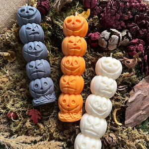 Può includere: Tre candele a forma di zucca impilate, una arancione, una bianca e una grigia. Ogni candela ha un viso di zucca intagliato diverso.