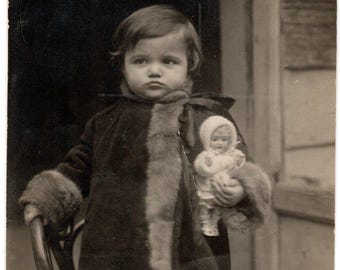 Retrato antiguo de un niño con una muñeca. Fotografía vintage. Foto de infancia con un toque melancólico. Decoración nostálgica de estilo europeo.