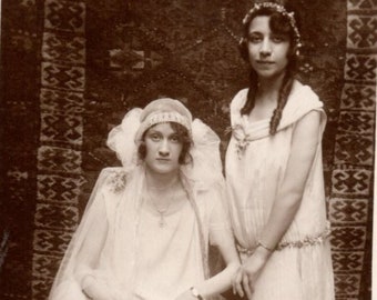 A Historical Bridal Photo, Vintage Fashion of the Bride and Her Friend in White, Taken in Front of the Traditional Carpet Decor