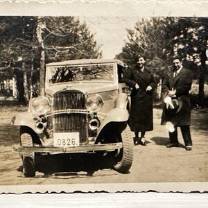 A Very Beautiful, Old Model Car And A Lady And Gentleman In Elegant Clothes With Hats Next To It.